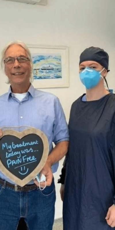 Patient Photos - Hampshire Dentists Pain Free Dentist in Southampton Patient with Dental nurse at Hampshire Dentists, holding a sign saying "My treatment today was pain free" emphasising pain-free dental care.