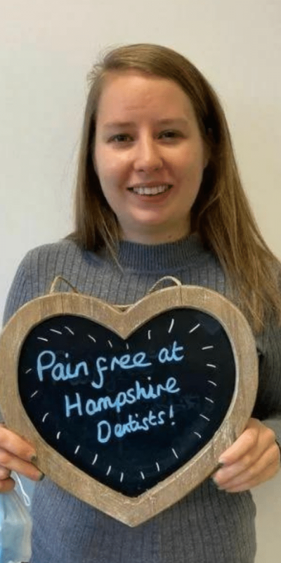 Patient Photos - Hampshire Dentists Pain Free Dentist in Southampton Patient at Hampshire Dentists, holding a sign saying "Pain free at Hampshire Dentists" emphasising pain-free dental care.