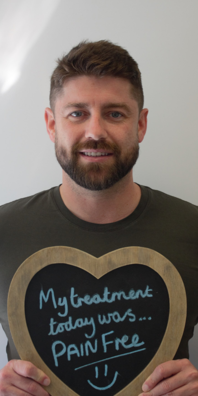 Patient at Hampshire Dentists, holding a sign saying " My treatment today was pain free " emphasising pain-free dental care.