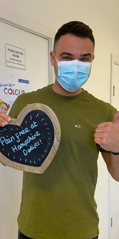 Patient at Hampshire Dentists, holding a sign saying "Pain free at Hampshire Dentists" emphasising pain-free dental care.