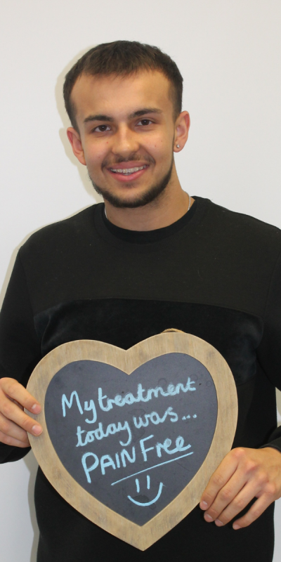 Patient at Hampshire Dentists, holding a sign saying " My treatment today was pain free " emphasising pain-free dental care.