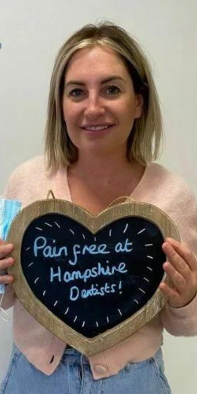Patient at Hampshire Dentists, holding a sign saying "Pain free at Hampshire Dentists" emphasising pain-free dental care.