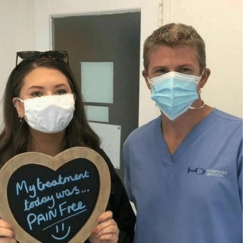 Dr Robin Hanna, Implantologist - Hampshire Dentists Pain Free Dentist in Southampton Patient with Dr Robin Hanna at Hampshire Dentists, holding a sign saying "My treatment today was pain free" emphasising pain-free dental care.