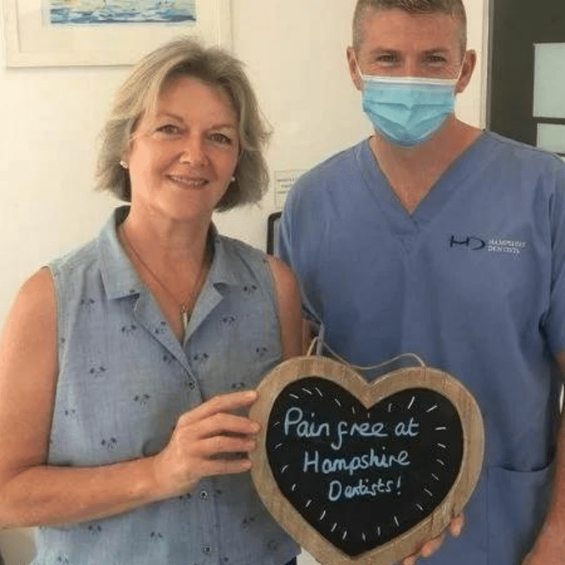 Dr Robin Hanna, Implantologist - Hampshire Dentists Pain Free Dentist in Southampton Patient with Dr Robin Hanna at Hampshire Dentists, holding a sign saying " Pain free at Hampshire Dentists" emphasising pain-free dental care.