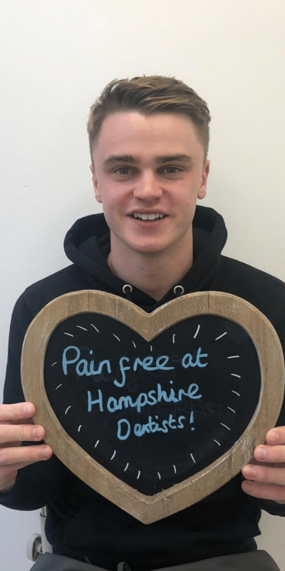 Patient Photos - Hampshire Dentists Pain Free Dentist in Southampton Patient at Hampshire Dentists, holding a sign saying "Pain free at Hampshire Dentists" emphasising pain-free dental care.
