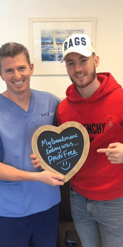 Patient Photos - Hampshire Dentists Pain Free Dentist in Southampton Patient with Dr Robin Hanna at Hampshire Dentists, holding a sign saying "My treatment today was pain free" emphasising pain-free dental care.